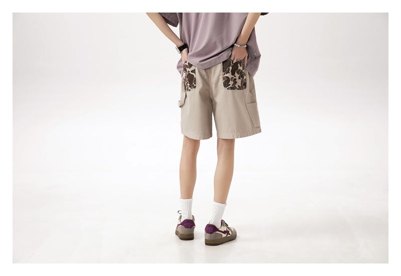 Cropped back view of a model wearing beige shorts with dark patterned back pockets and side cargo pockets.