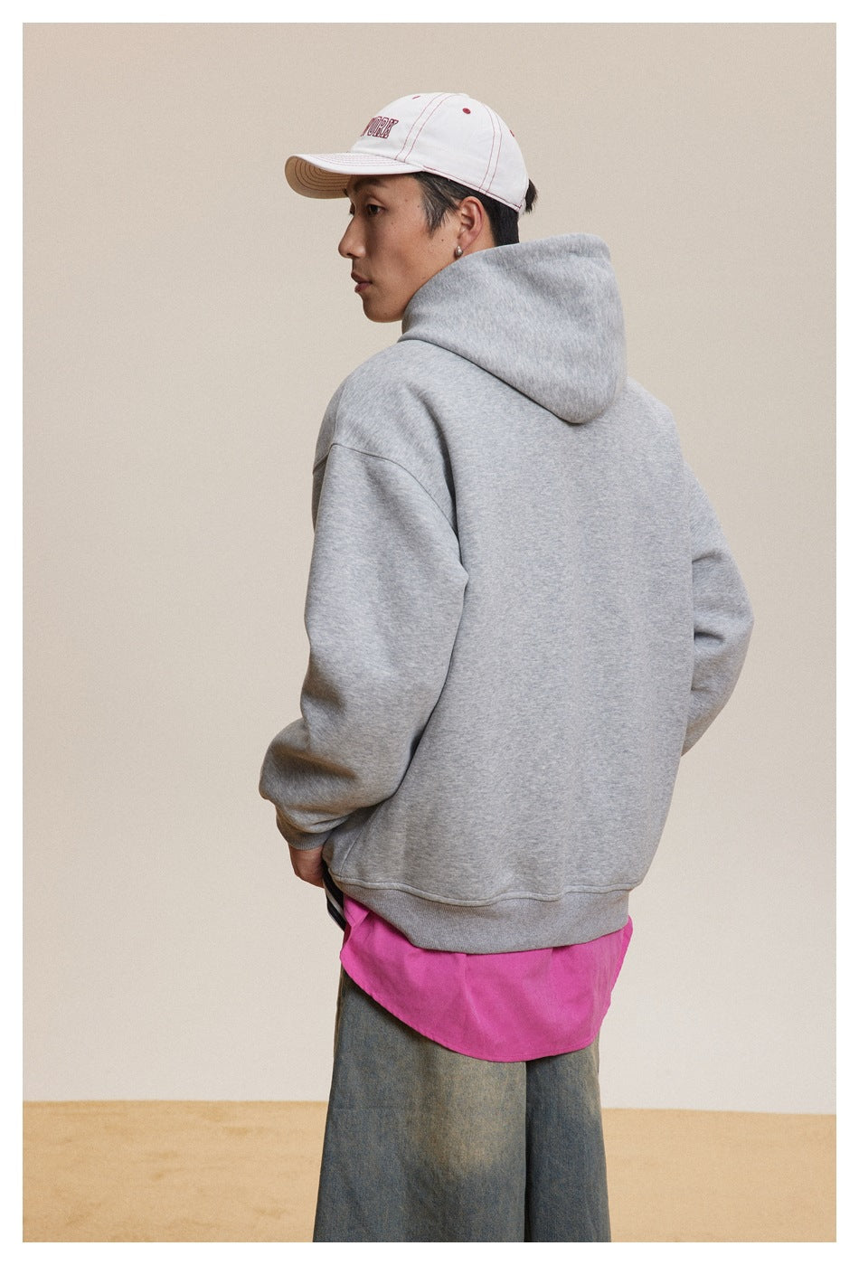 Rear view of a model wearing a plain gray hooded sweatshirt over a bright pink shirt.