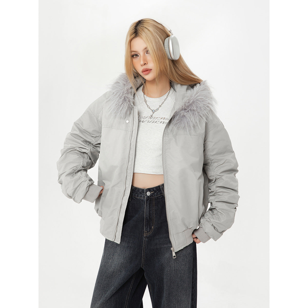 Model wearing a light gray fur-collar jacket open over a cropped top and dark jeans.