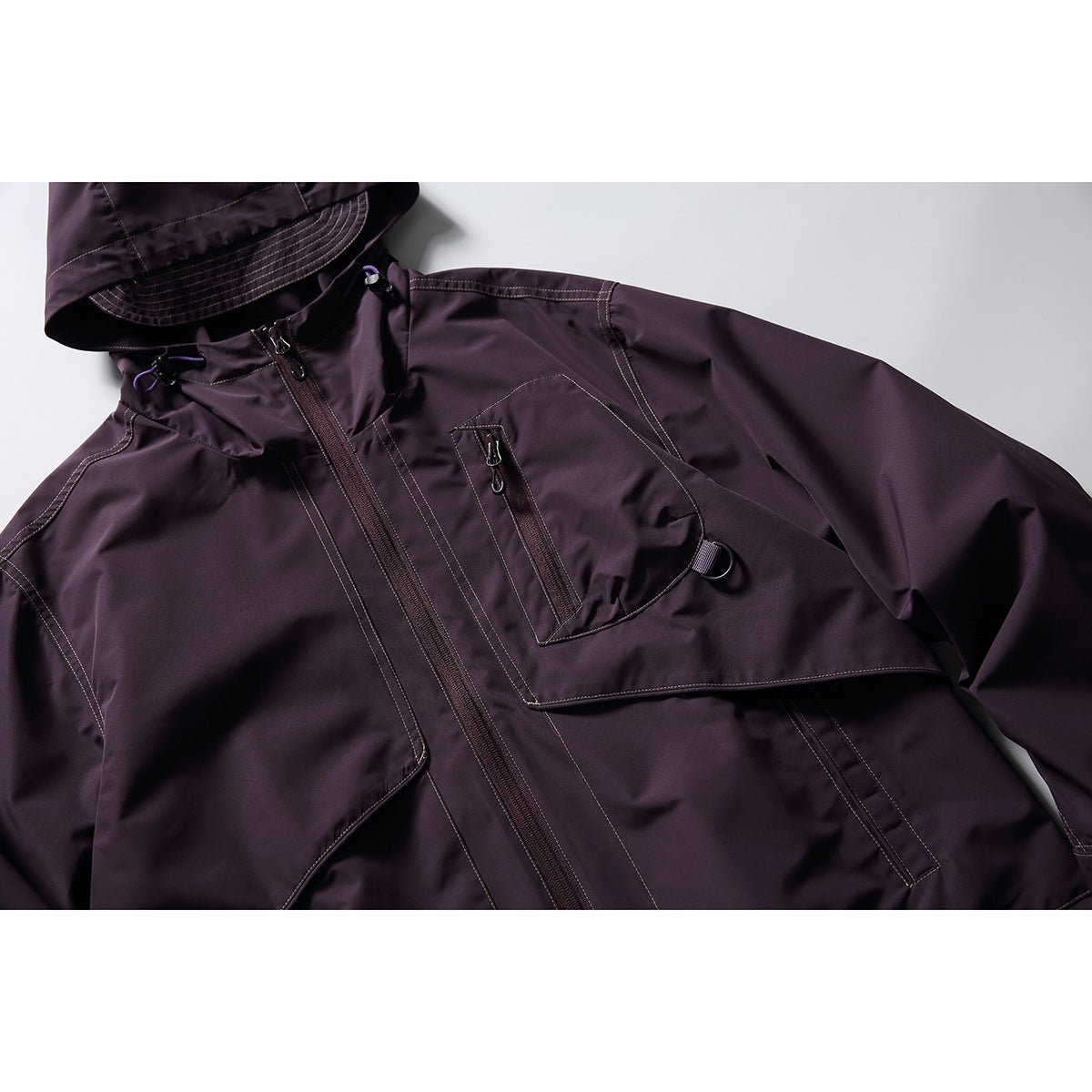 Close-up of a dark plum hooded jacket showing the hood, front zipper, chest pockets and contrast stitching.