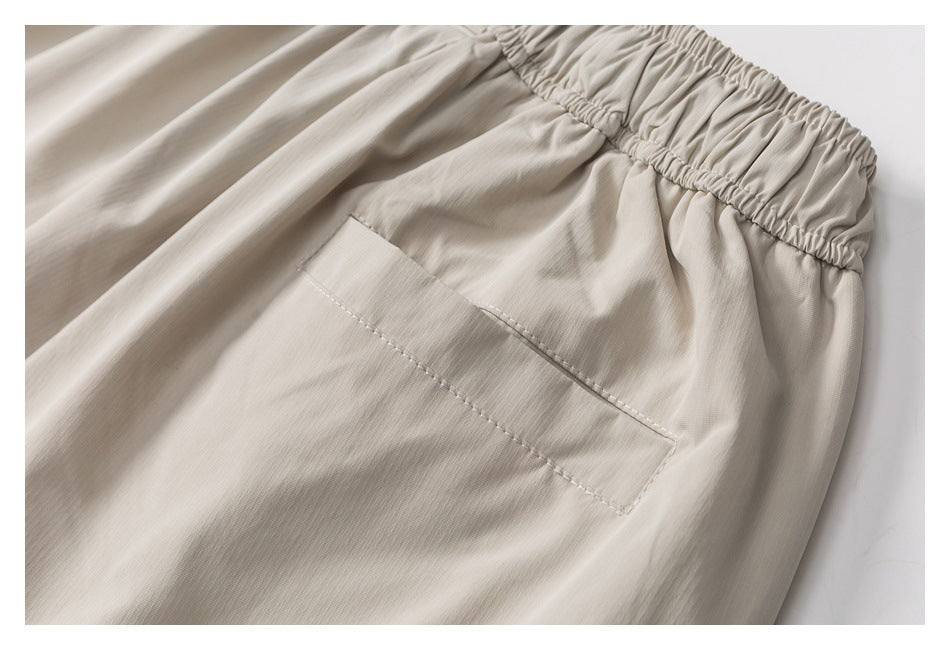 Close-up of a large stitched pocket below the gathered elastic waistband of a light beige garment.