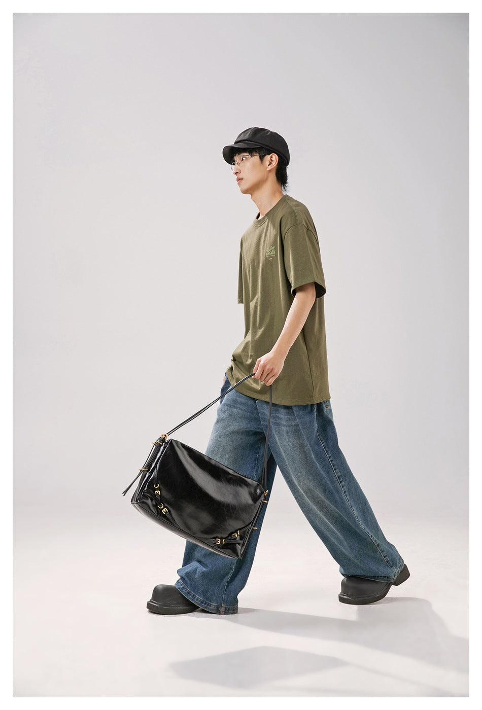 Model walking in an olive-green short-sleeve T-shirt and wide-leg jeans, side view, carrying a black shoulder bag