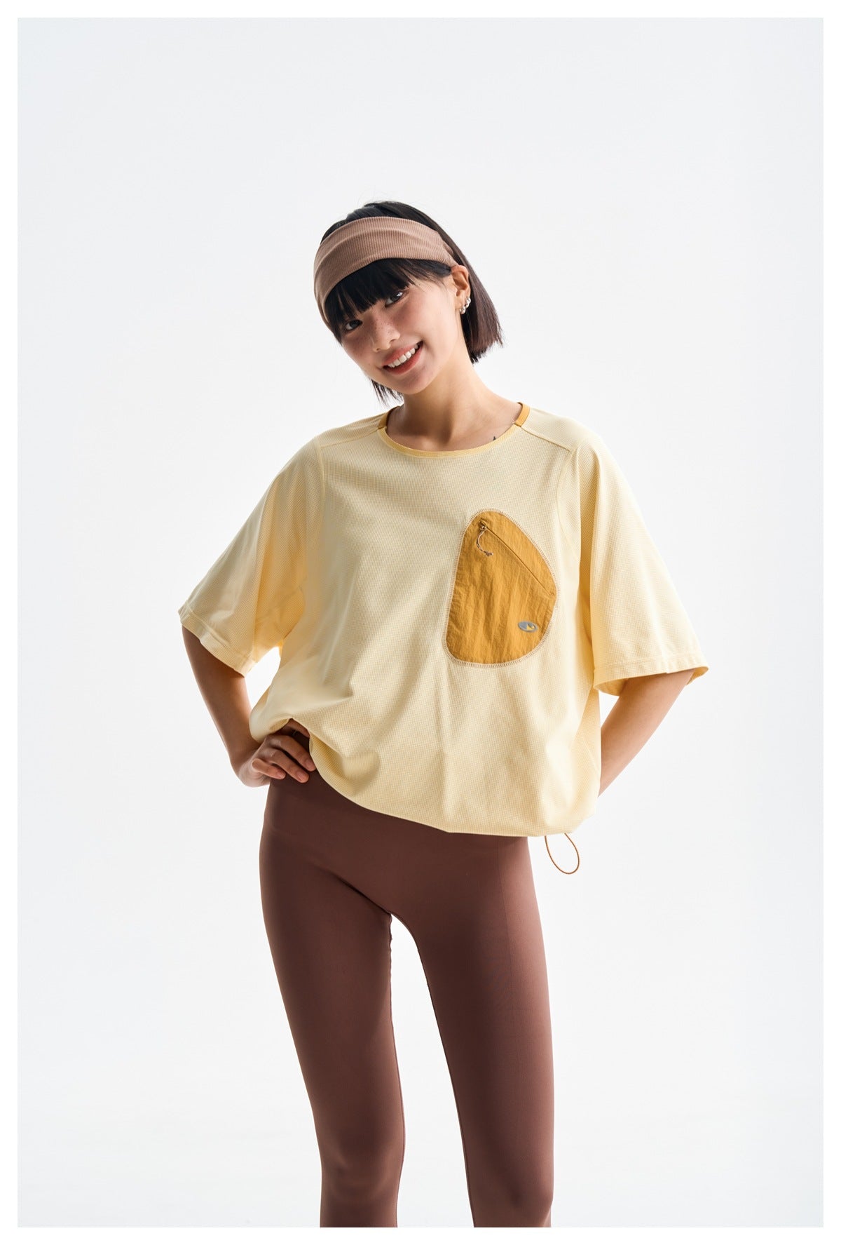 Front view of a model wearing a pale yellow oversized tee with a large tan patch pocket and brown leggings.