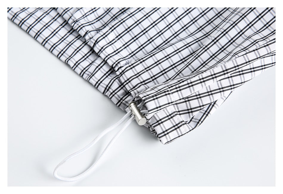 Close-up of a white drawcord and metal toggle at the edge of black-and-gray plaid fabric.