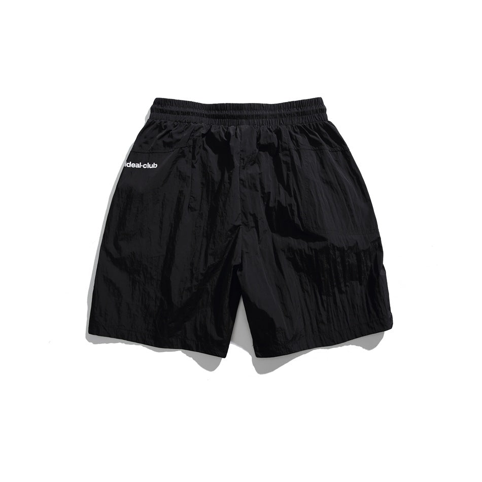 Black flat-lay shorts with an elastic waistband, loose legs, and small white “ideal-club” lettering.