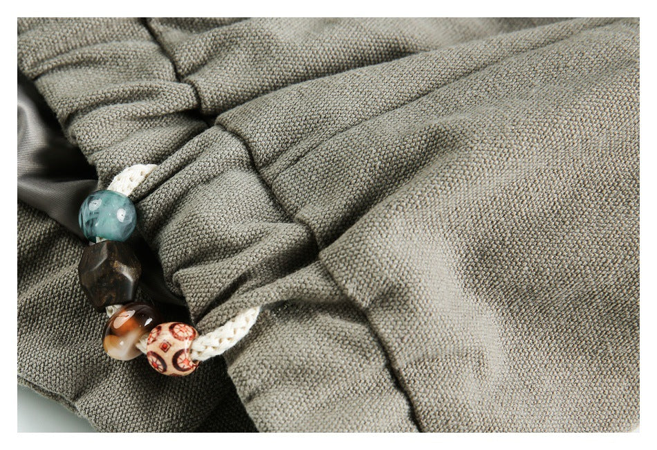 Close-up of gathered gray-khaki fabric with a braided cord and decorative beads.
