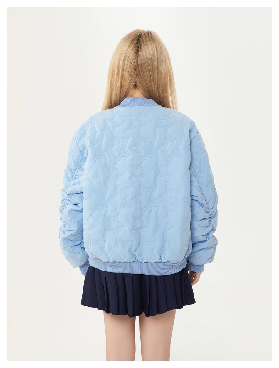 Back view of a model wearing a light blue star-quilted bomber jacket with ribbed trim and a navy pleated skirt.
