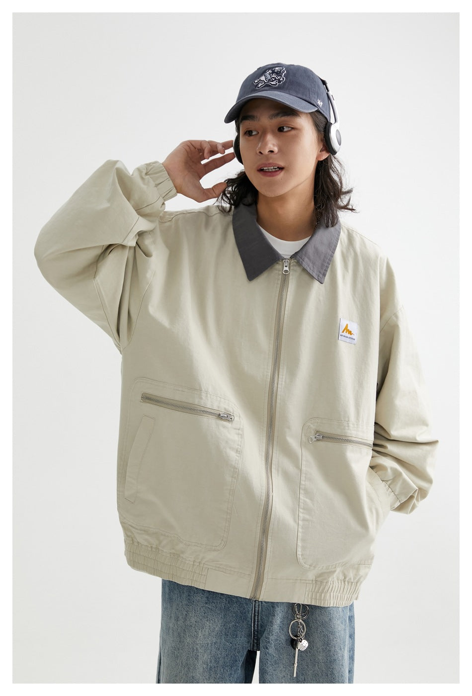 Model wearing a light khaki zip jacket with a gray collar, roomy sleeves, and large front pockets.
