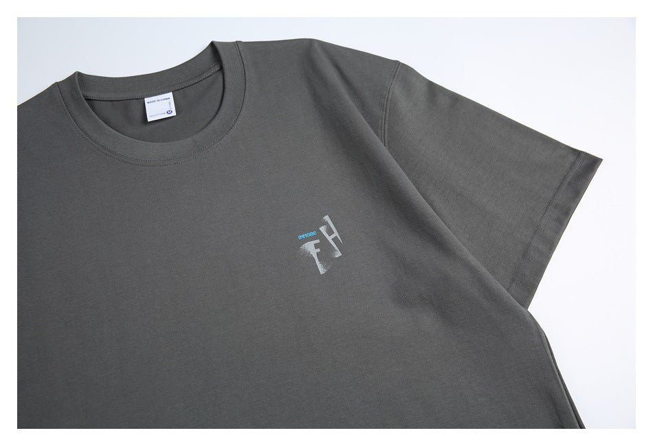 Close view of the charcoal gray T-shirt front, showing its crew neck, short sleeve, and small gray-and-blue chest graphic.