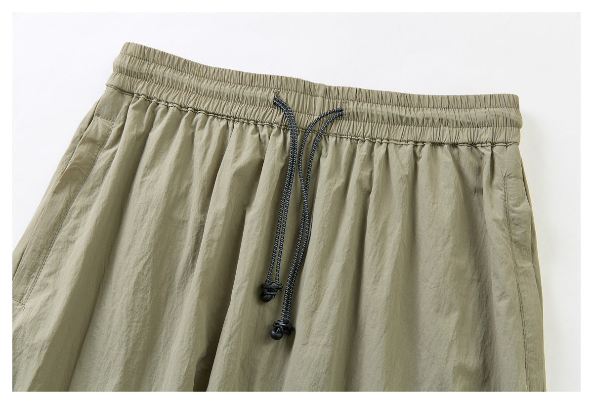 Close-up of a khaki garment's elastic waistband, dark drawcords, and side pocket edges.