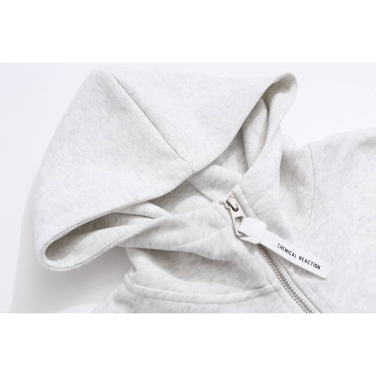 Close-up of a light gray hood and silver quarter-zipper with a white pull tab reading “CHEMICAL REACTION.”