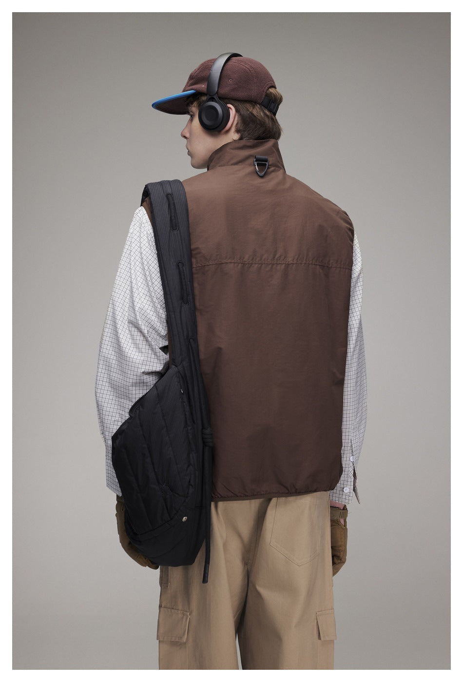Back view of a model wearing a brown vest over a checked shirt with khaki pants and a black quilted bag
