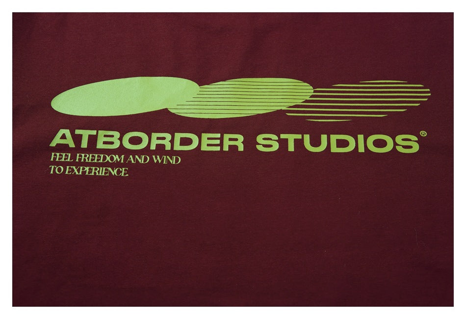Close-up of burgundy fabric with a lime-green ATBORDER STUDIOS logo and tagline.