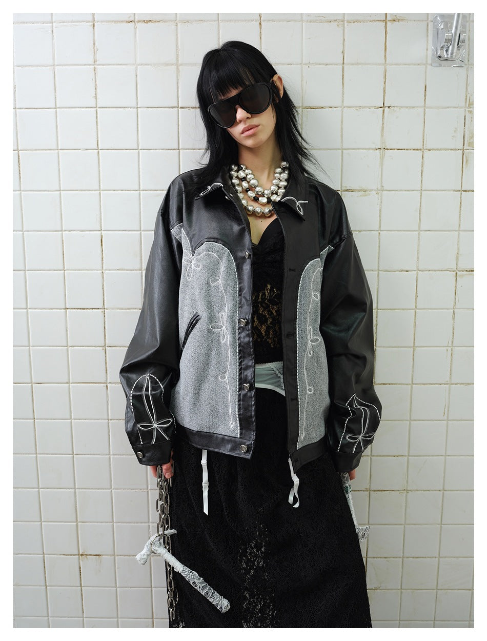 Model wearing black and gray embroidered jacket with embroidered cuffs over black lace, against white tile wall