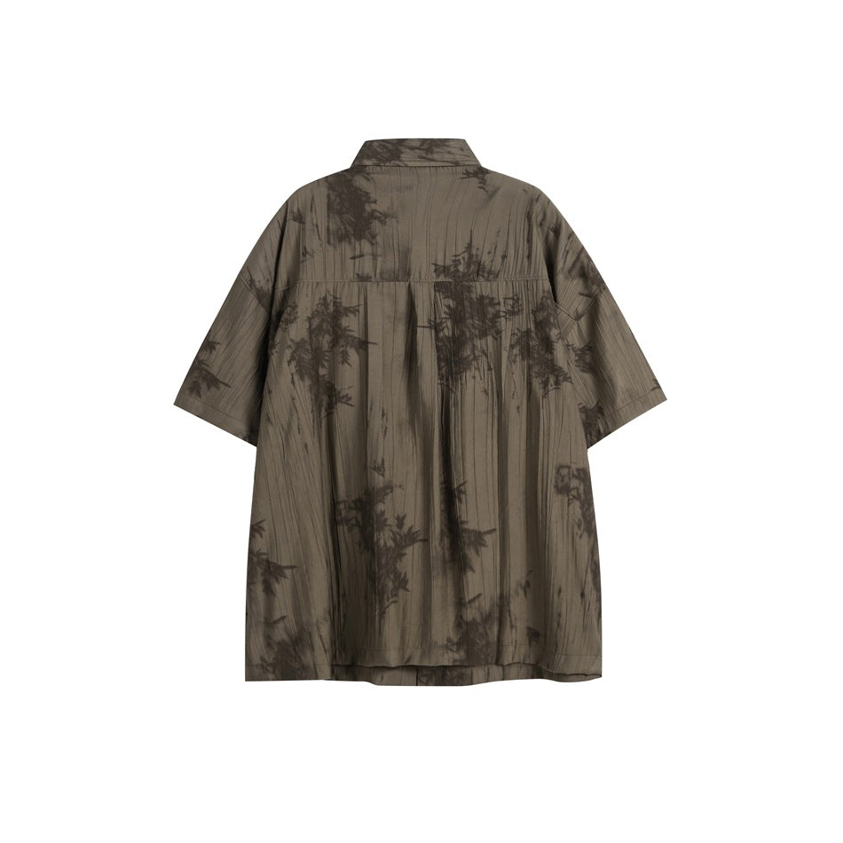 Back view of a loose dark taupe short-sleeve shirt with a collar and dark botanical pattern.