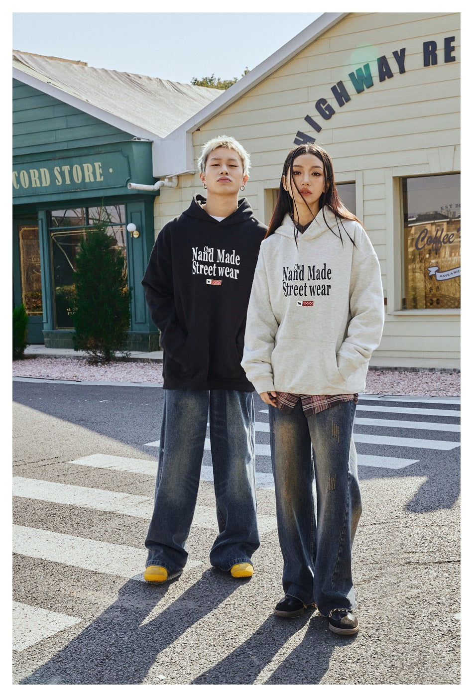 Two models wear black and light gray graphic pullover hoodies with kangaroo pockets, styled with loose jeans.