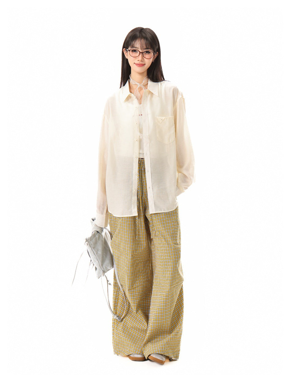 Woman wearing an open beige button-up shirt over a tank top with yellow plaid wide-leg pants, holding a gray bag