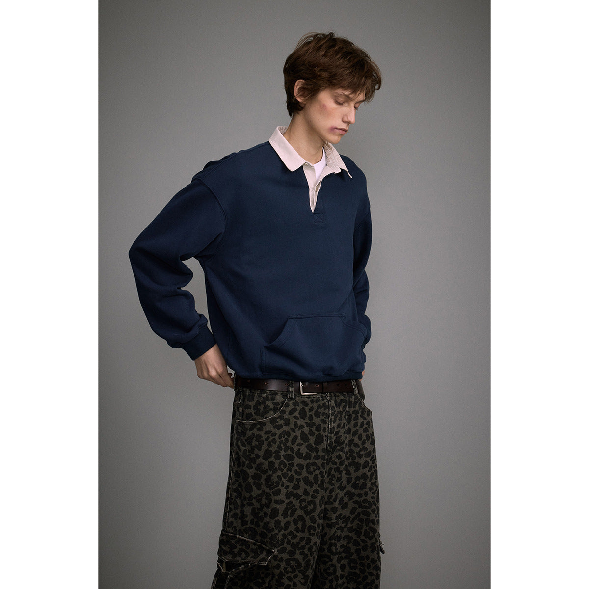 Model wearing a navy pullover with a pale pink collar and kangaroo pocket, paired with dark leopard-print cargo pants.