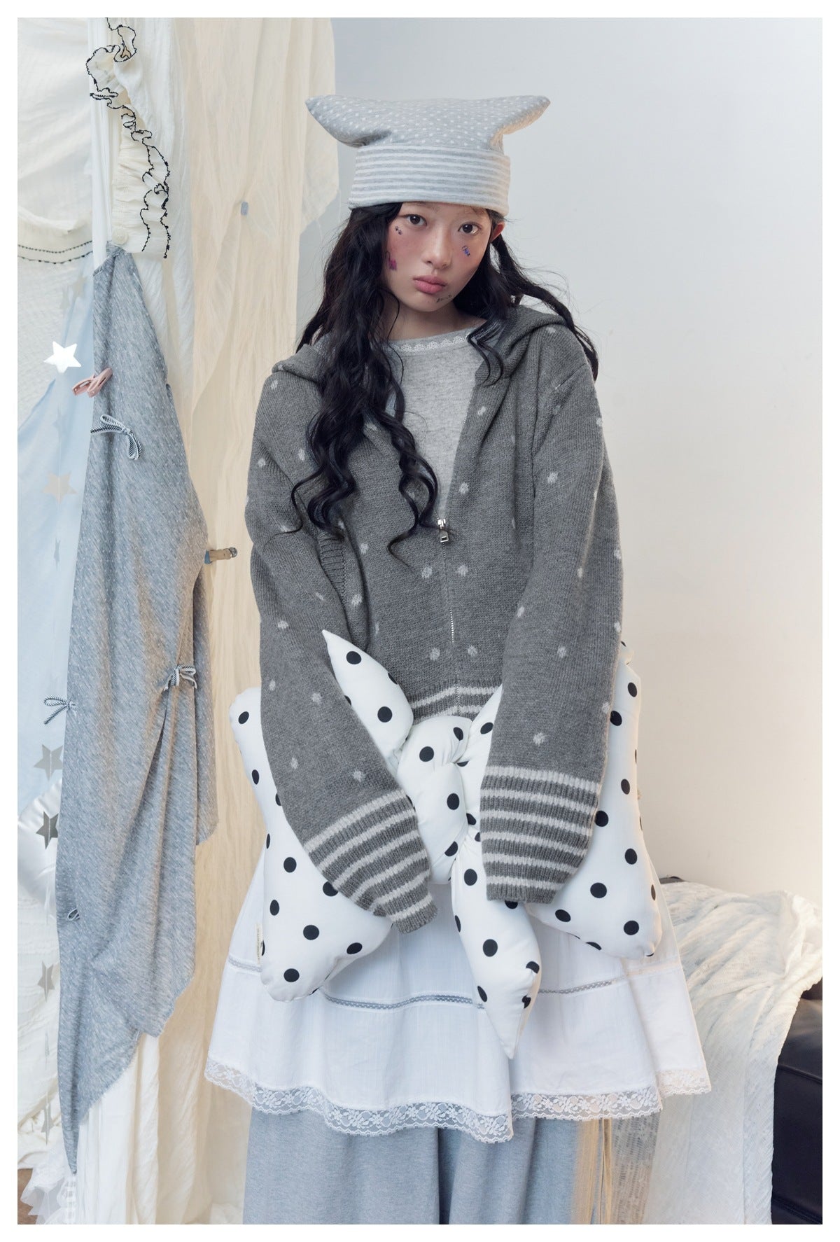 Model wearing a gray hooded zip cardigan with small white motifs and striped cuffs over a white lace-trim dress.