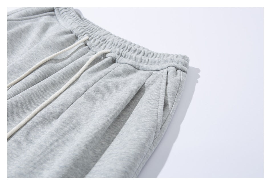 Angled close-up of light gray sweatpants showing the gathered waistband, white drawstrings, and side pocket opening.