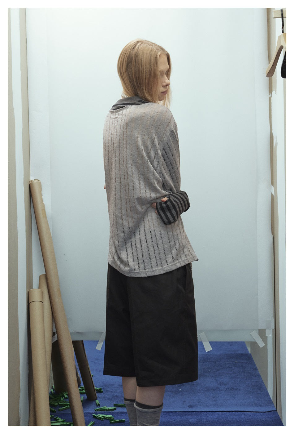 Back view of a model wearing a loose gray T-shirt with thin vertical stripes and dark striped sleeves, paired with black