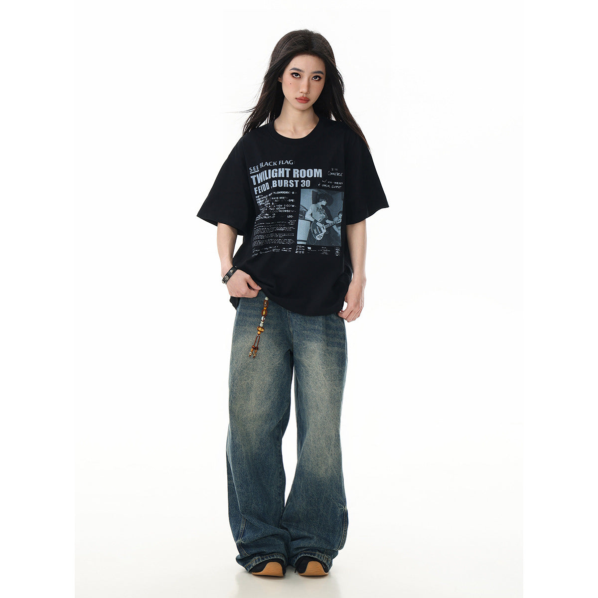 Model wearing a black oversized graphic T-shirt with a gray concert-poster-style print and loose blue jeans.