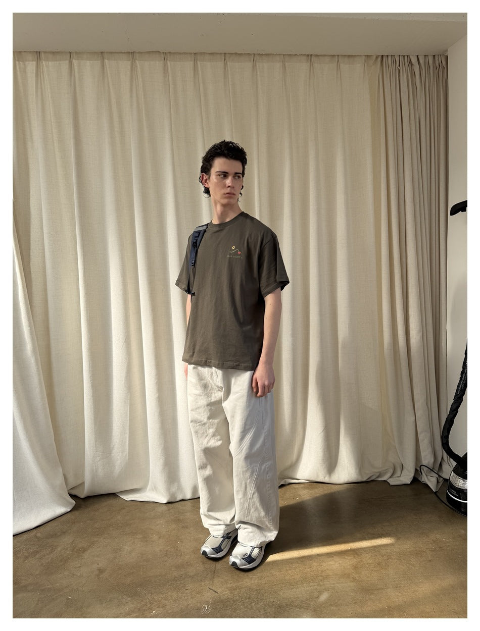 Angled view of a model wearing a dark olive graphic T-shirt and loose white pants.