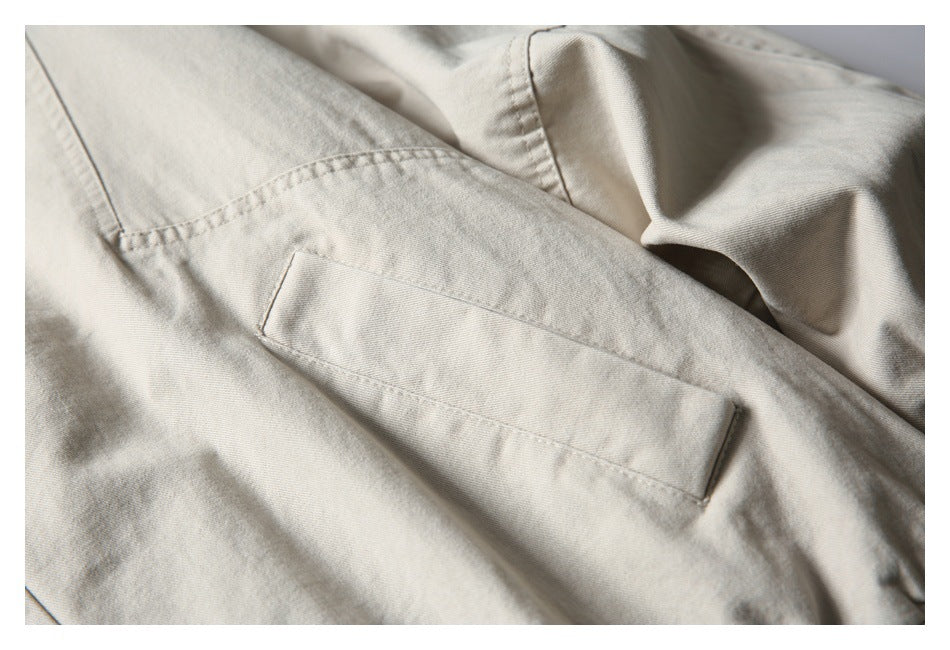 Close-up of a light beige jacket with a rectangular stitched pocket and visible seams.