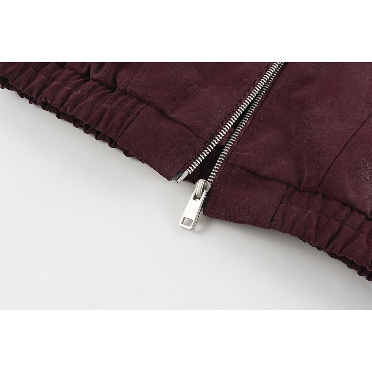 Close-up of the burgundy jacket's gathered hem and silver front zipper.