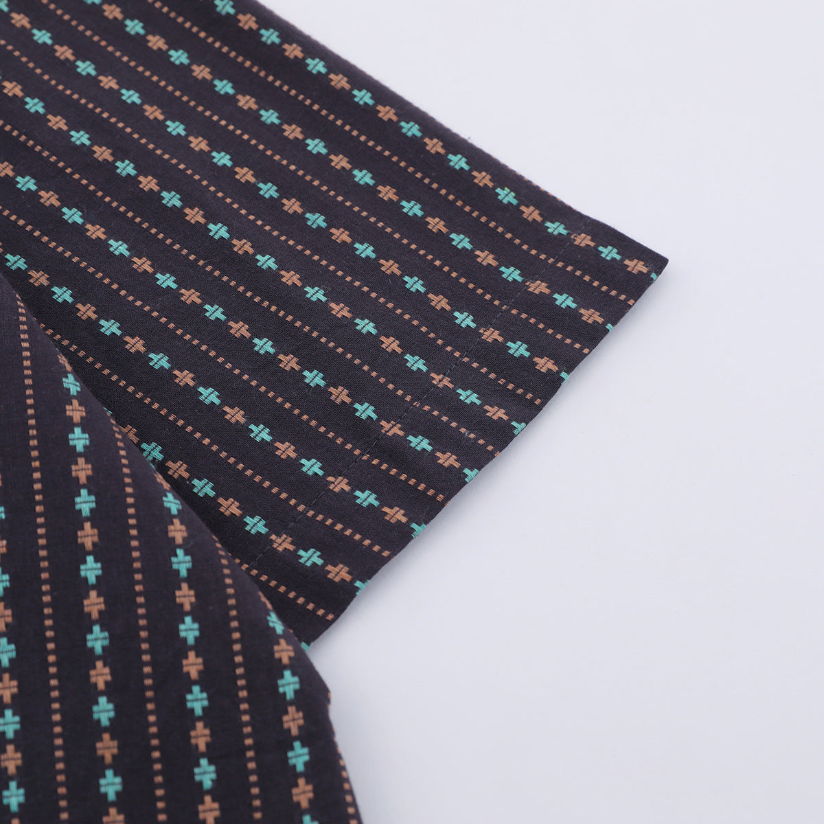 Close-up of a short sleeve on a dark shirt with turquoise and rust motifs and dotted stripes, against a white background.