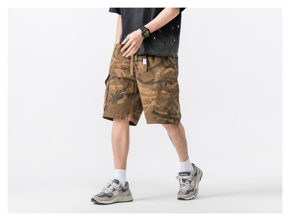 Model wearing tan and brown camouflage cargo shorts, shown from a slight front-side angle.