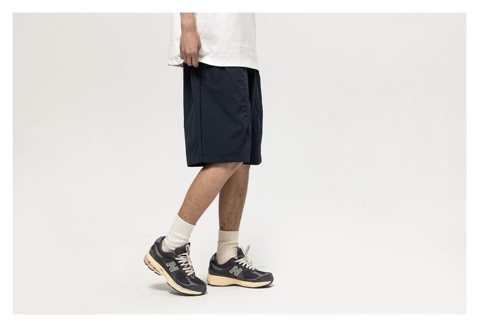 Cropped side view of a model wearing dark navy knee-length shorts, a white T-shirt, and sneakers.