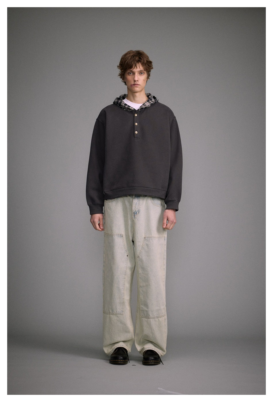 Model wearing a dark gray plaid-hood henley hoodie with light washed wide-leg jeans and black boots, front view