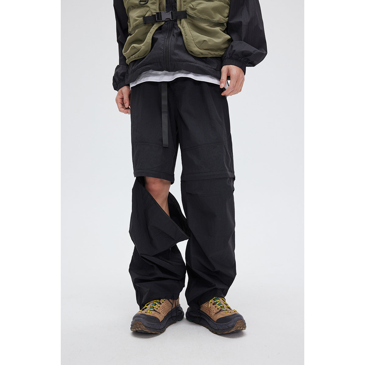 Cropped front view of a model wearing black convertible pants with shorts and one lower leg section unfastened.