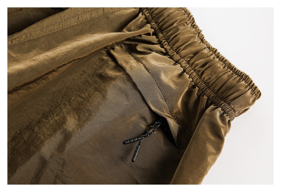 Close-up of brown trousers showing the gathered elastic waistband and a black drawcord at the pocket opening.