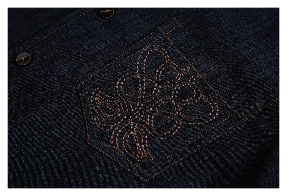 Close-up of a dark denim patch pocket with a brown embroidered floral motif and orange stitching.