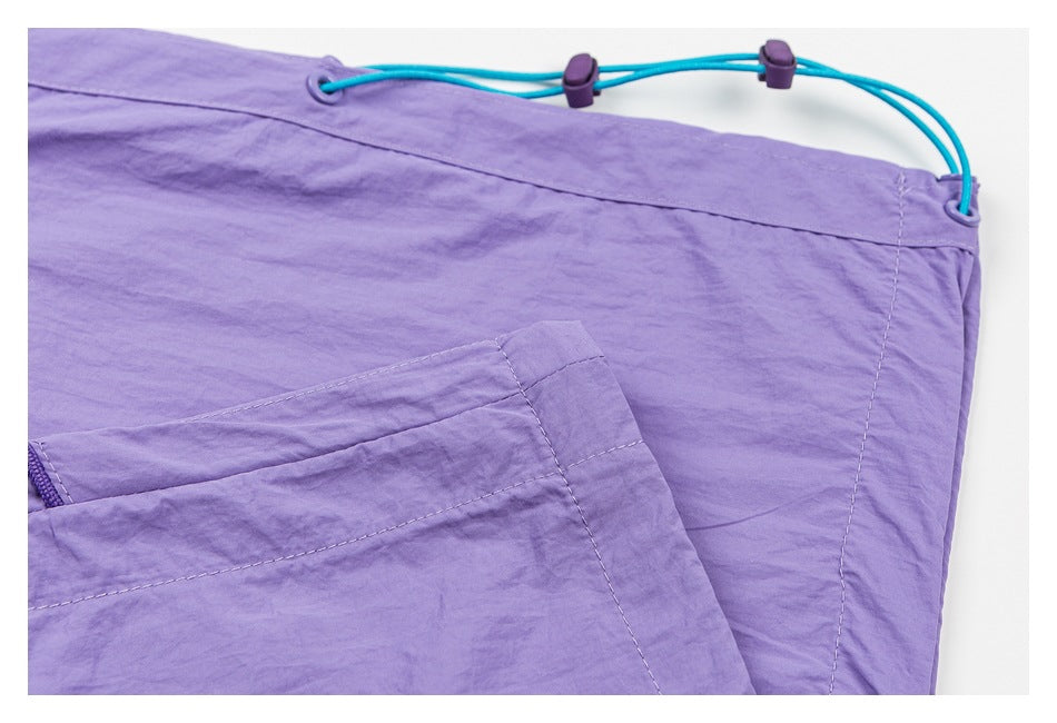 Close-up of lavender pants showing a turquoise adjustable waist cord, purple toggles, and part of a pocket.