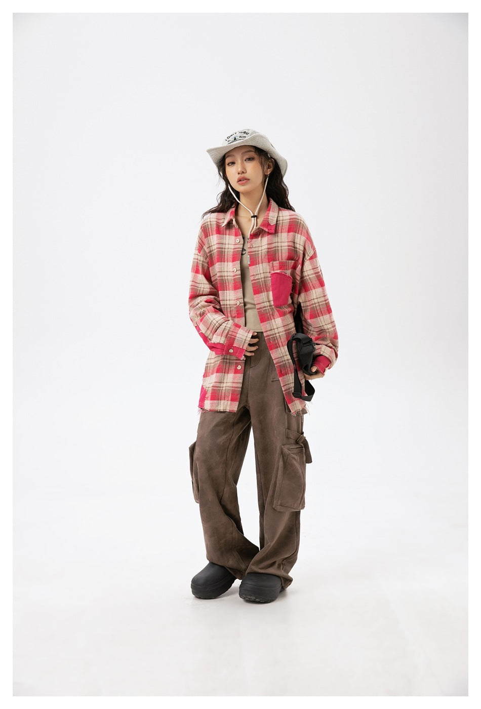 Model wearing an oversized beige and red plaid button-up shirt with a bright pink chest pocket and sleeve accents.