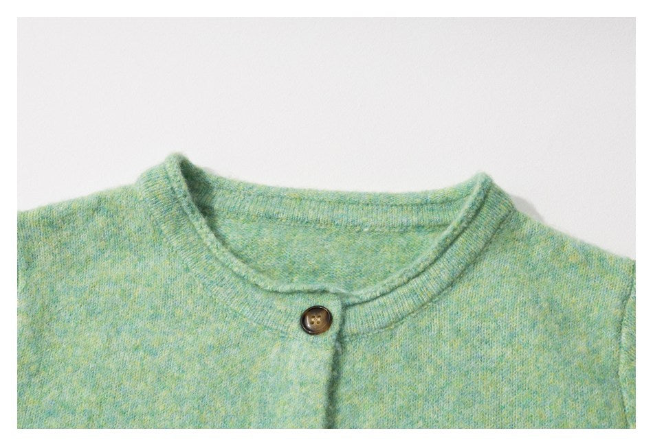 Close-up of the round neckline and a dark button on a mint green mottled cardigan.