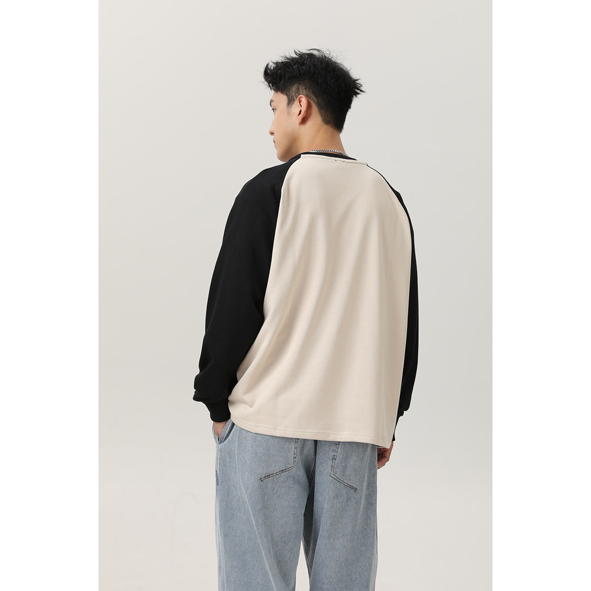 Rear view of a model wearing a cream sweatshirt with black raglan sleeves and loose light-wash jeans.