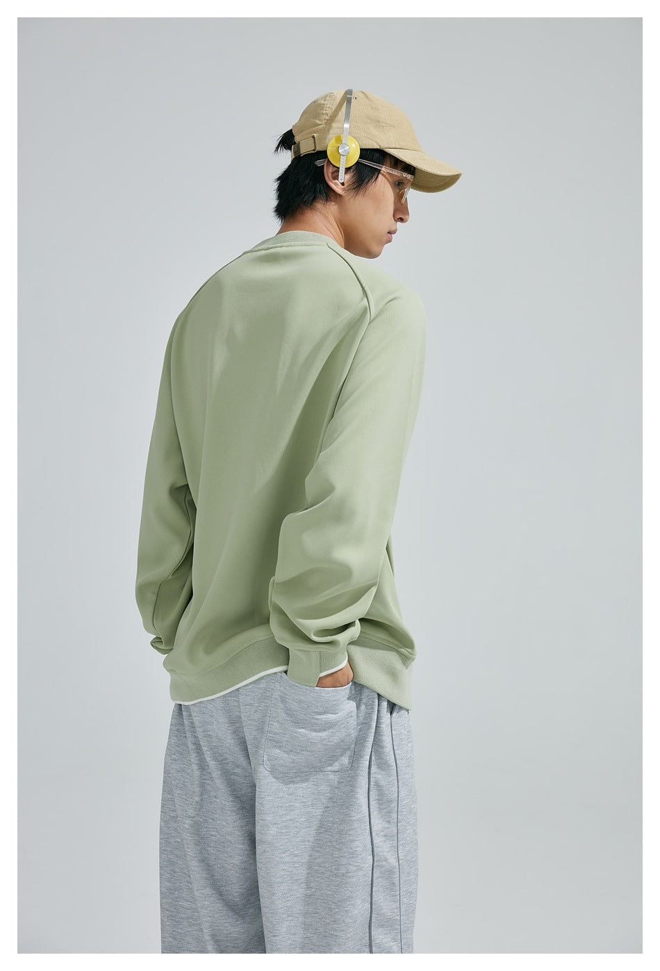 Side and back view of a model wearing a plain sage-green sweatshirt with ribbed cuffs and hem.