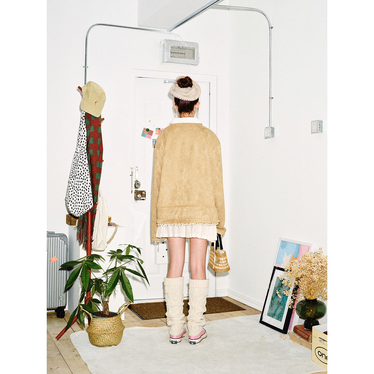 Back view of a model wearing a tan jacket with patterned hem trim over a short white skirt.