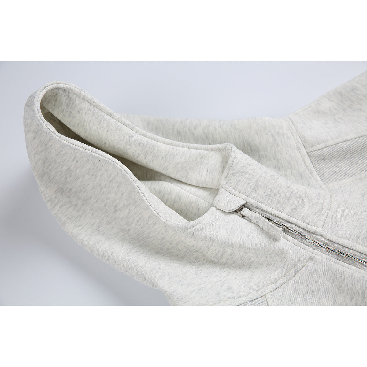 Close-up of a light heather gray hoodie showing the hood opening, short front zipper, and stitched panels.