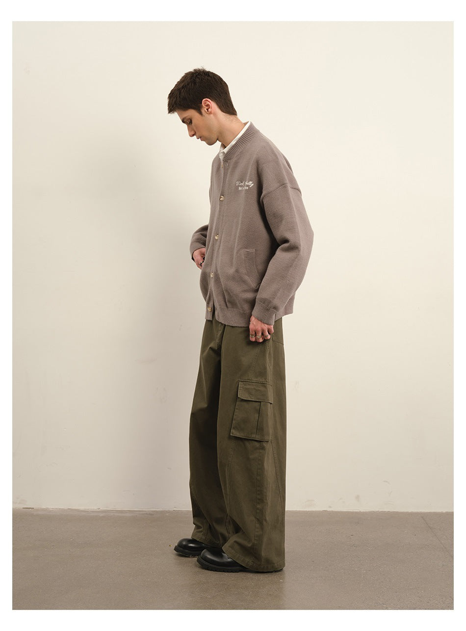 Side view of a model wearing a taupe button-front cardigan with embroidered lettering and olive cargo trousers.