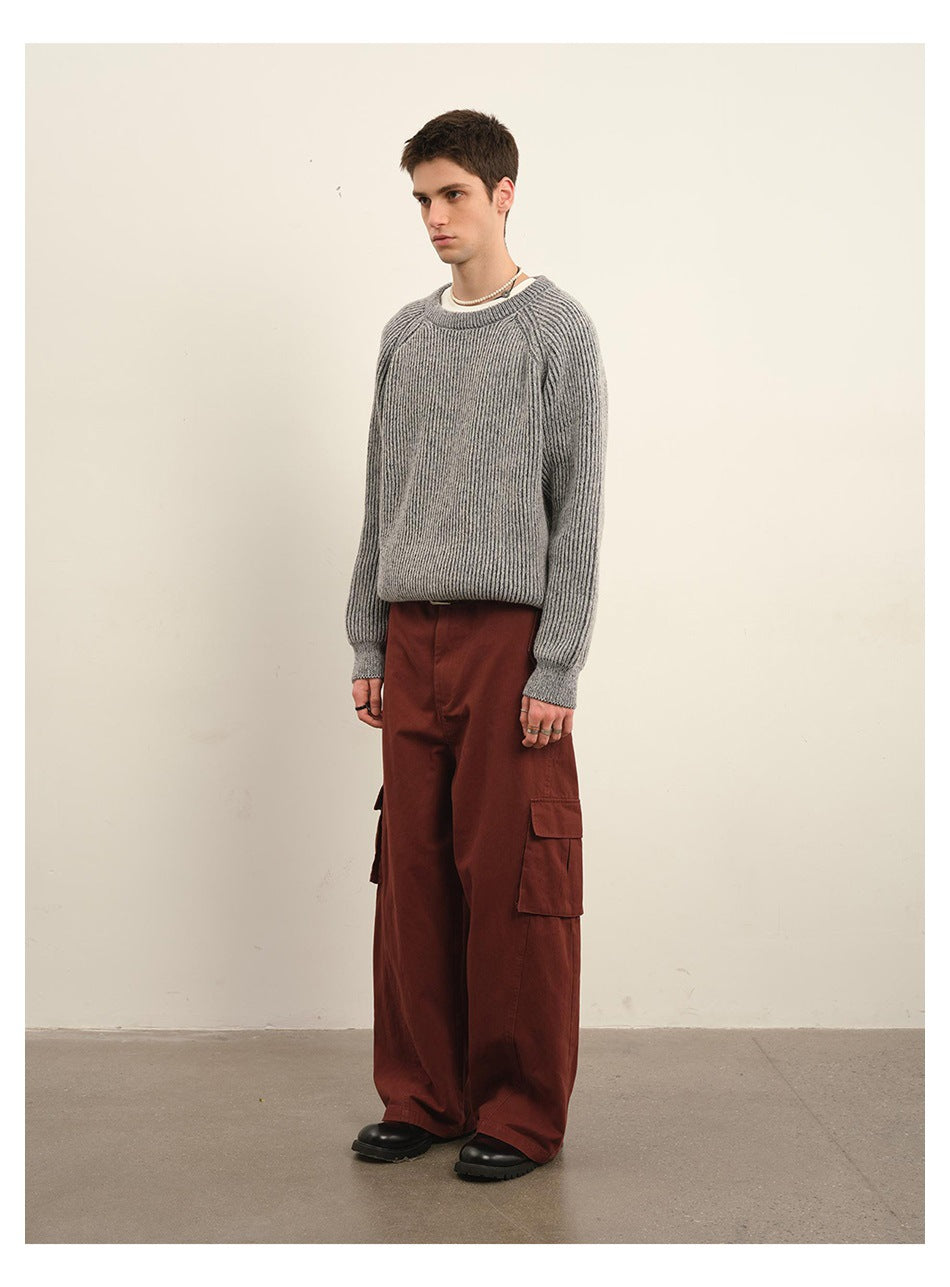 Male model in a gray ribbed crewneck sweater and rust-red cargo pants, shown at a three-quarter angle.