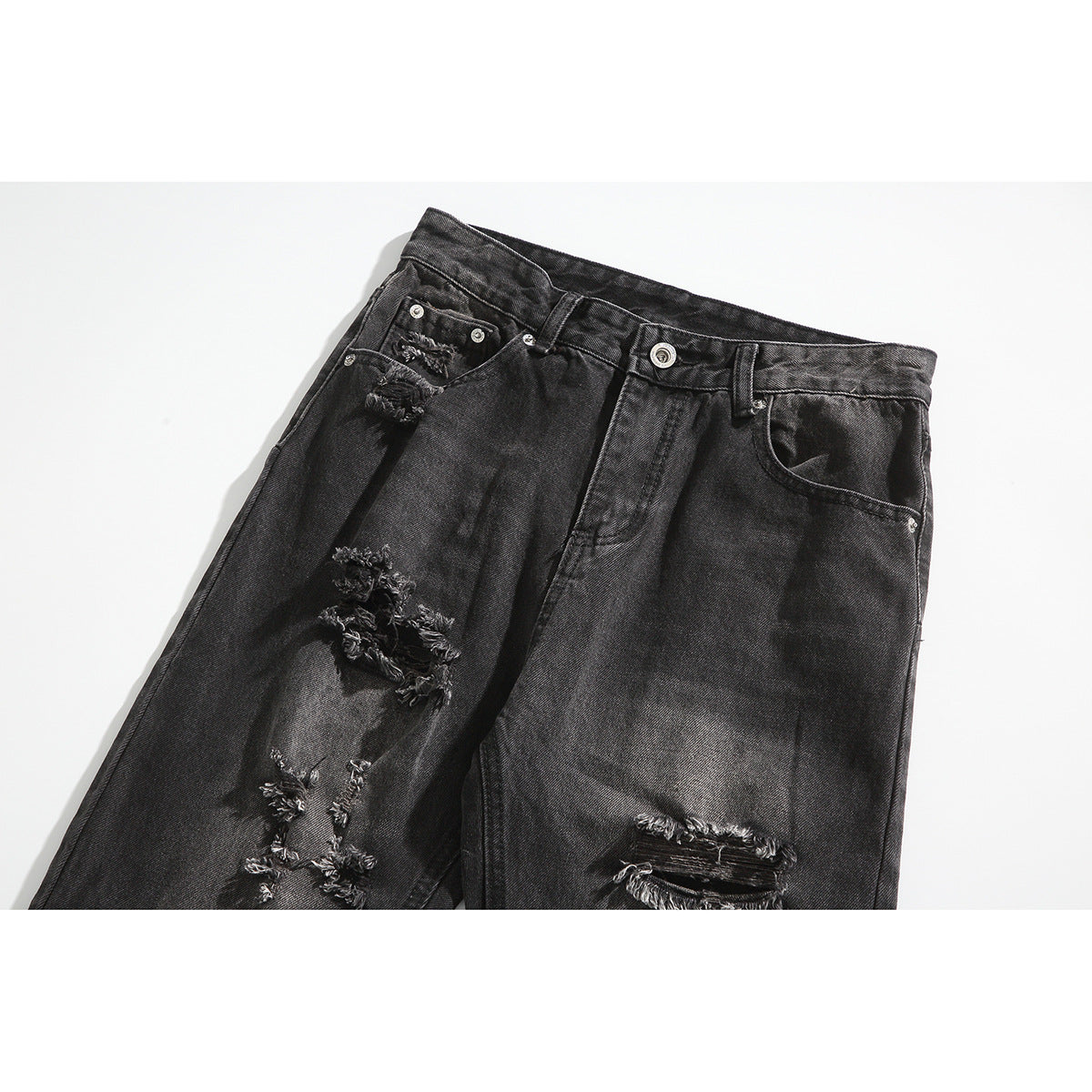 Close-up of black washed jeans showing the button fly, front pockets and multiple distressed tears.