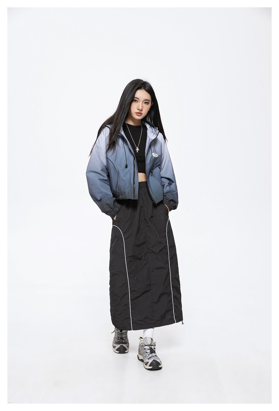 Full-length model wearing a blue-gray gradient hooded jacket with a black top and long black skirt.