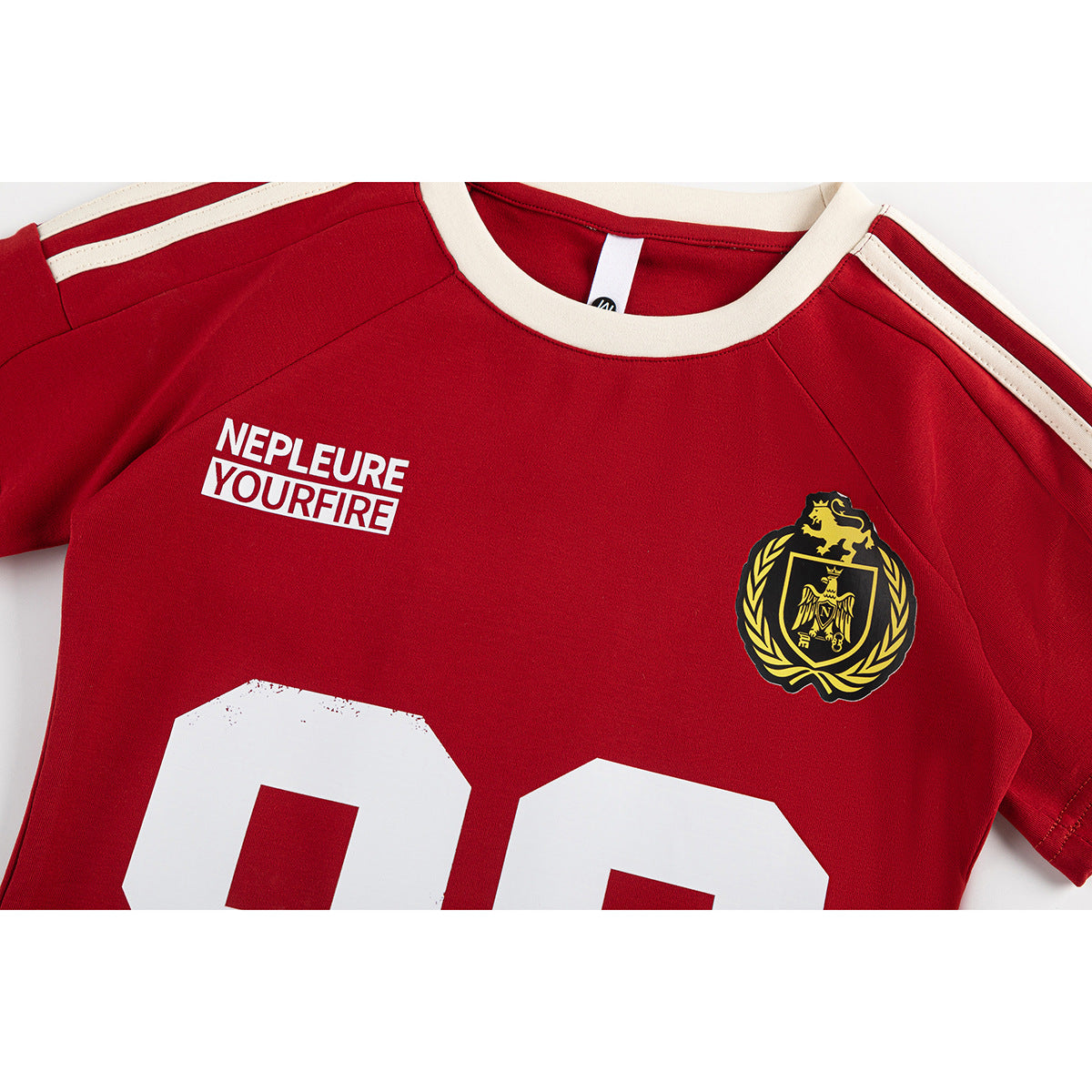 Close-up of a red jersey front with cream collar and shoulder stripes, white lettering, a gold crest, and part of a large