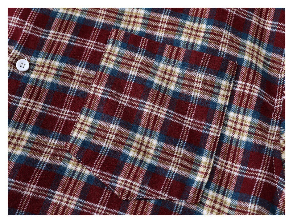 Close-up of a plaid shirt pocket and white button on burgundy, navy, cream, and tan checks.