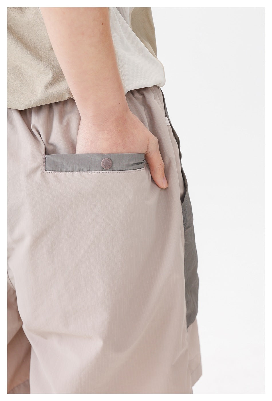 Close-up of a gray-trimmed pocket with a button on pale taupe shorts.